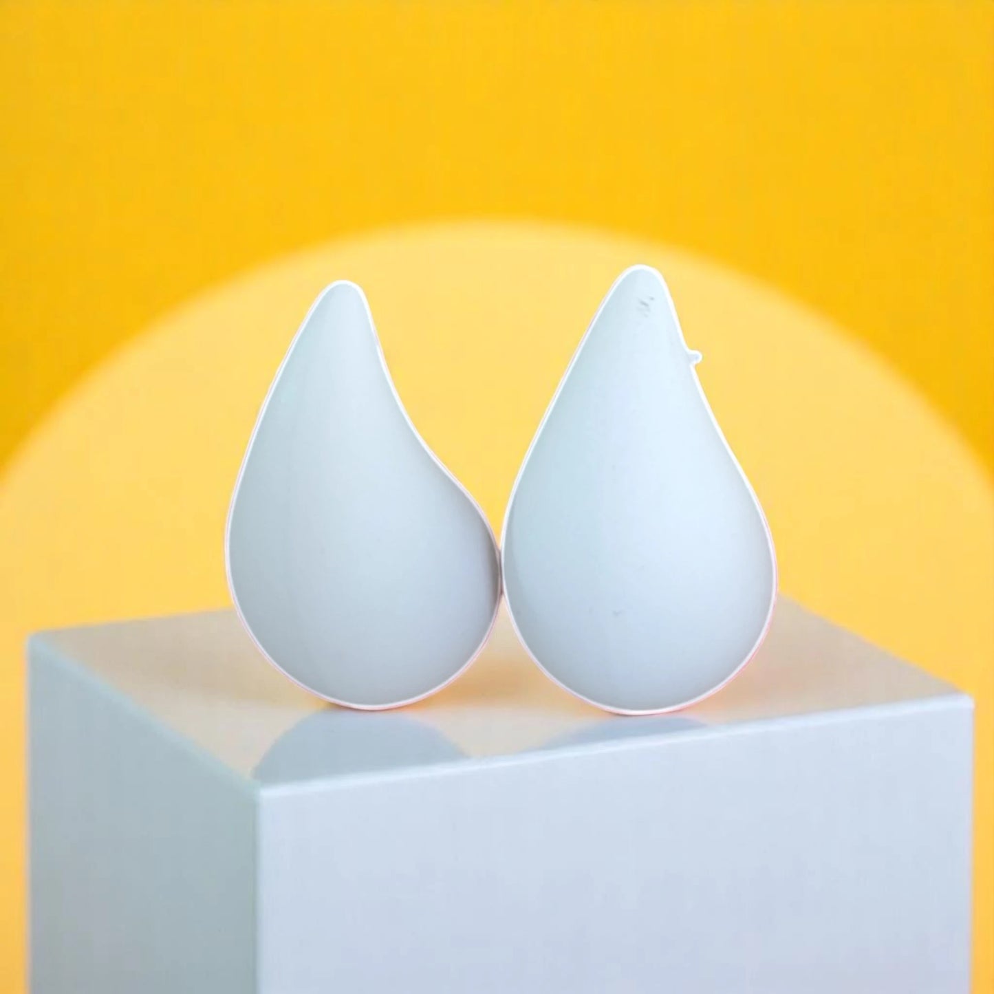 Two modern, white teardrop-shaped objects on a white pedestal against a bright yellow background, resembling minimalist design elements.