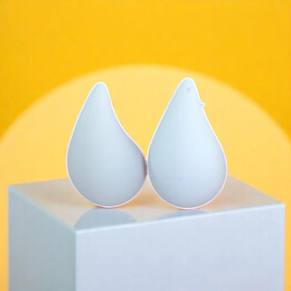 Two modern, white teardrop-shaped objects on a white pedestal against a bright yellow background, resembling minimalist design elements.