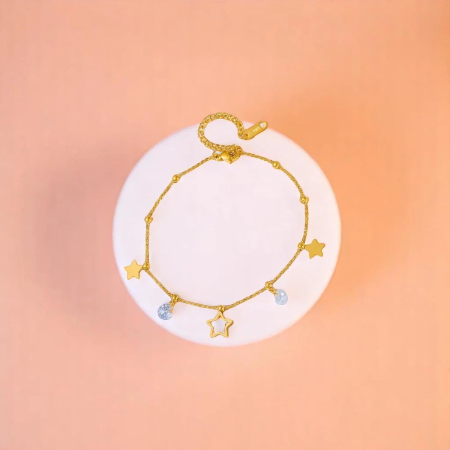 Anklet on geometric prop with peach color gradient in the background.