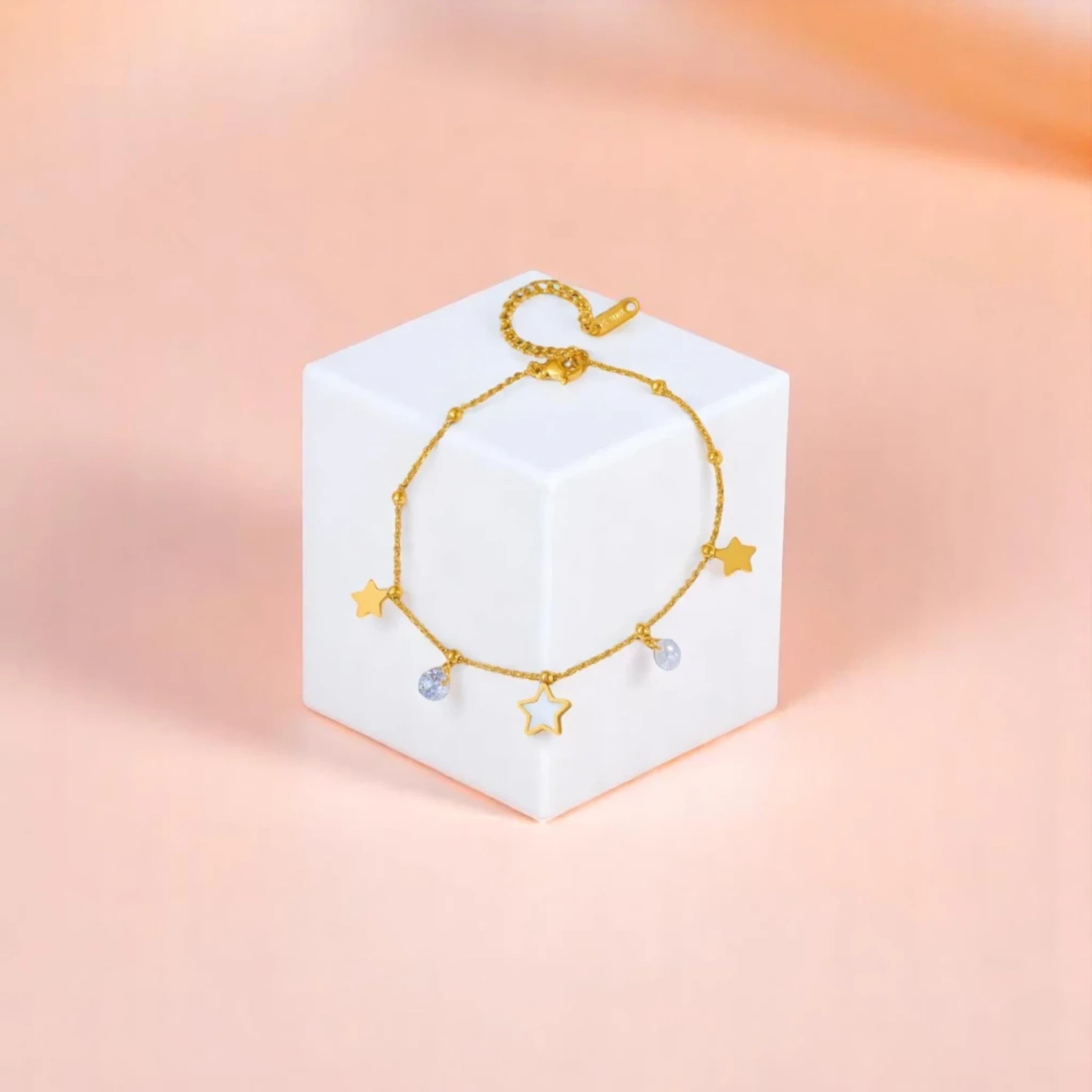 Anklet on geometric prop with peach color gradient in the background.