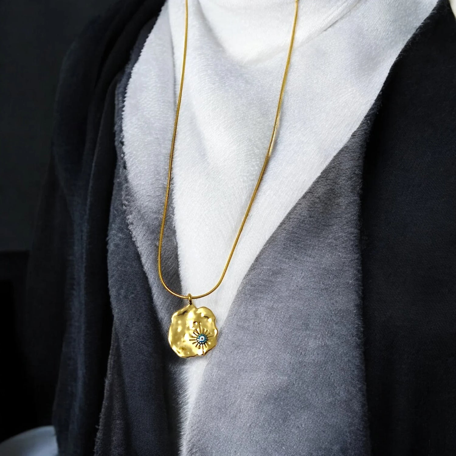 A close-up of a person wearing a gold pendant necklace with a turquoise stone, draped in a grey and black layered outfit.