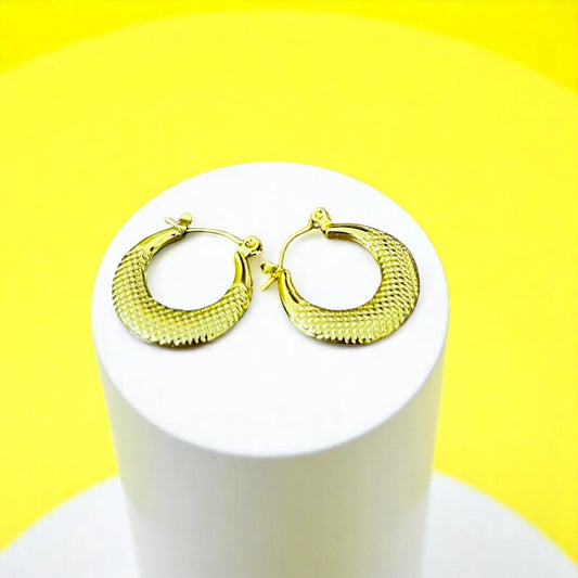 Stylish gold hoop earrings with a textured finish displayed on a white pedestal against a bright yellow background.