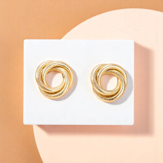 Gold hoop earrings arranged in a double twisted knot design, set against a minimalist background.