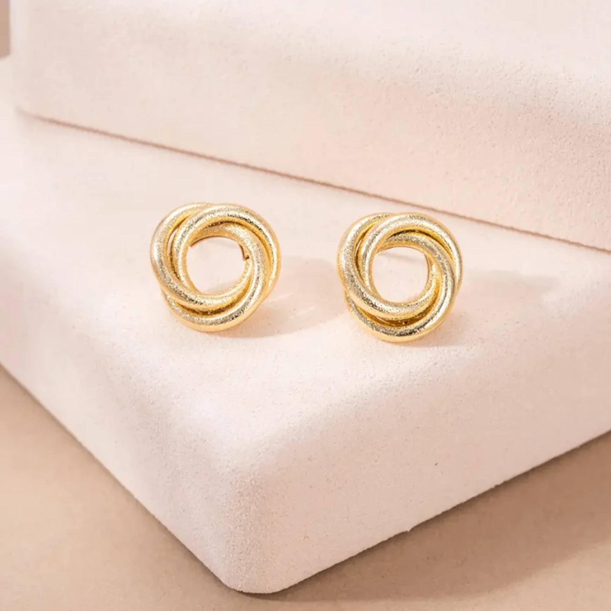 Gold knot-shaped earrings resting on a soft display, showcasing a sophisticated and elegant design.