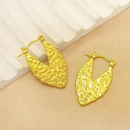 Gold hoop earrings with a textured, leaf-like design, elegantly displayed on a soft fabric background.