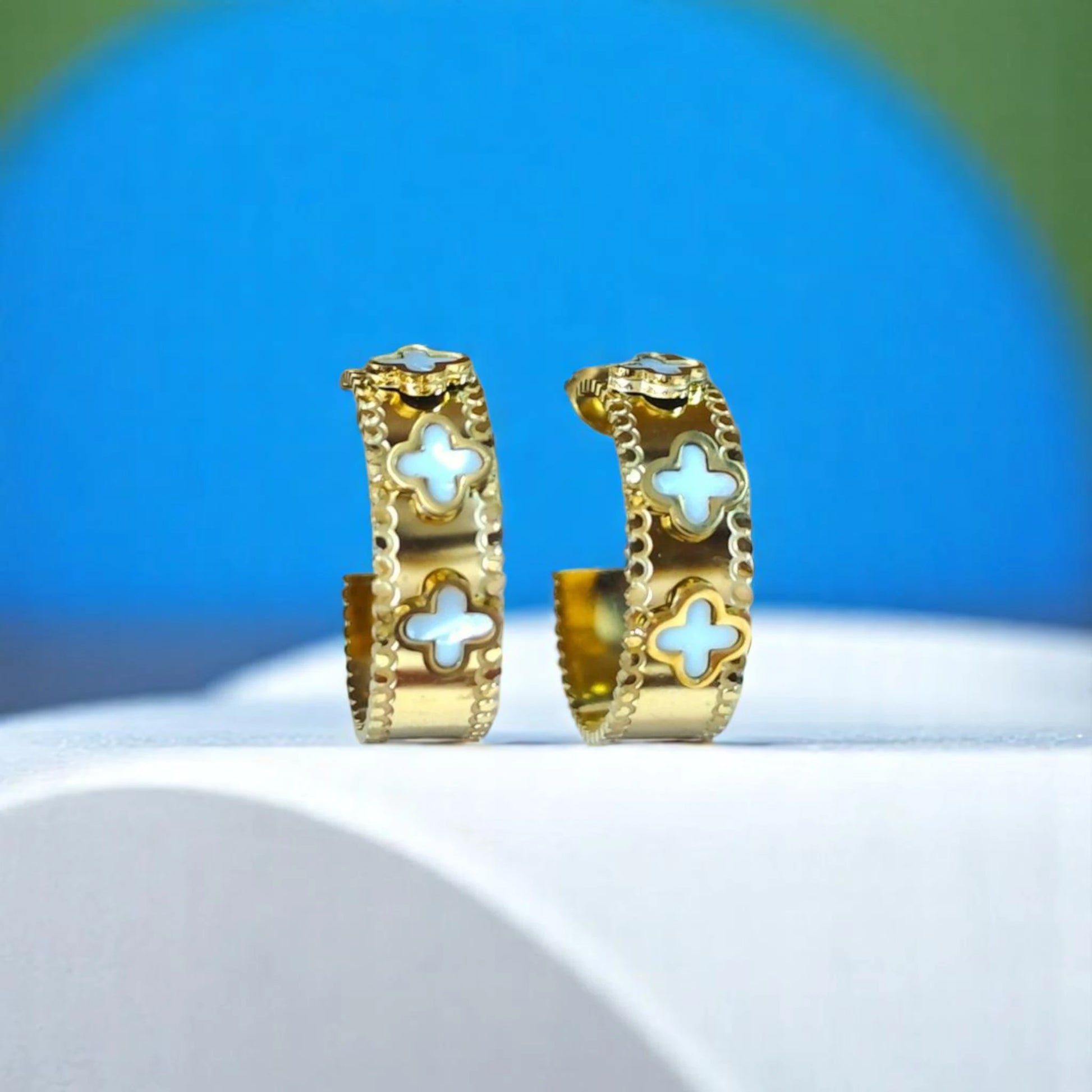 Gold hoop earrings featuring intricate cutouts with turquoise cross designs, displayed against a colorful backdrop.