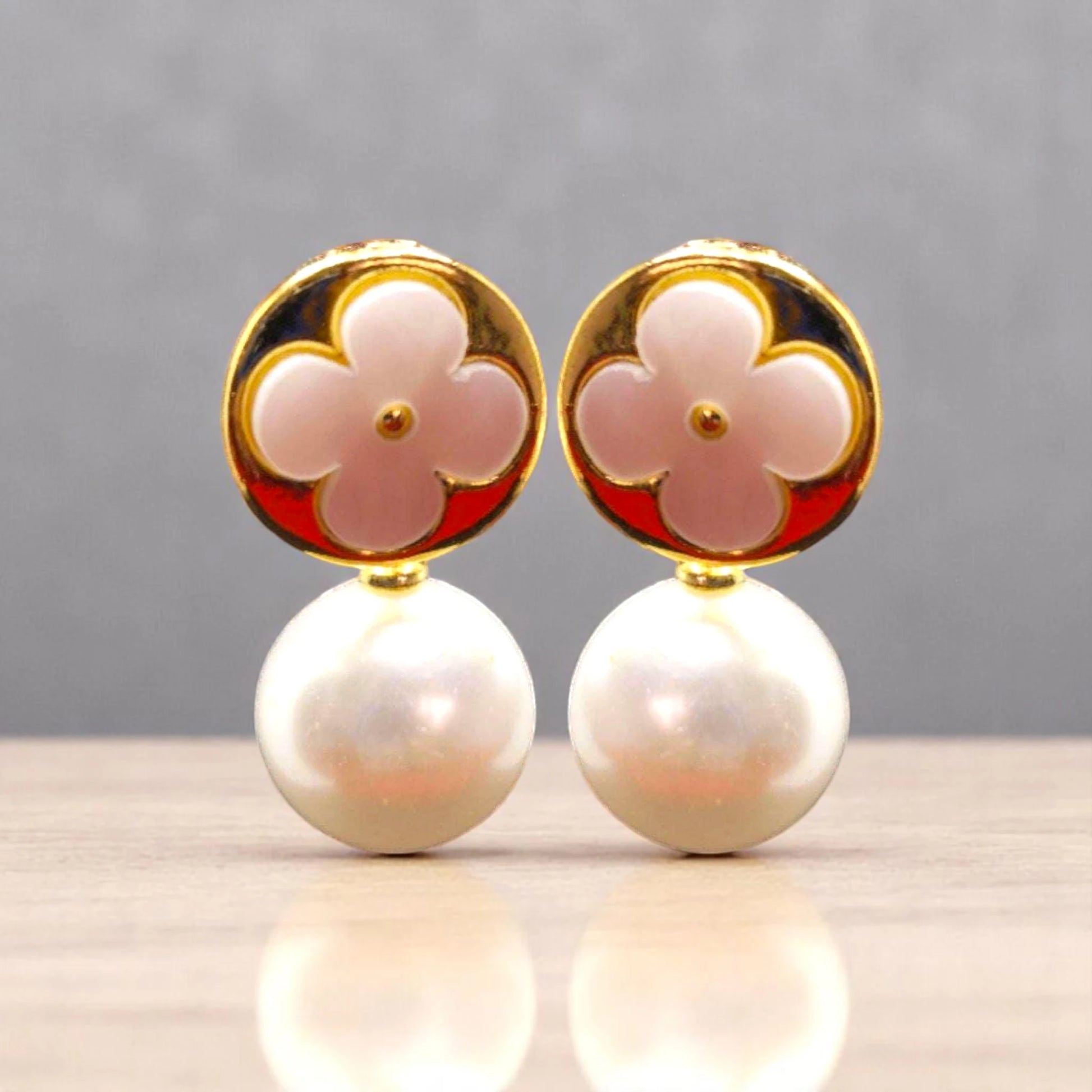 Elegant earrings featuring a pink flower design atop a lustrous pearl, set in gold, against a neutral backdrop.