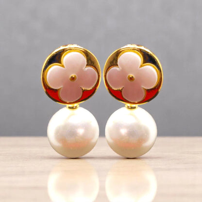 Elegant earrings featuring a pink flower design atop a lustrous pearl, set in gold, against a neutral backdrop.