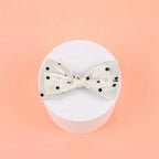 Bow with black polka dots on a white acrylic pedestal with a light background