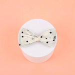Bow with black polka dots on a white acrylic pedestal with a light background