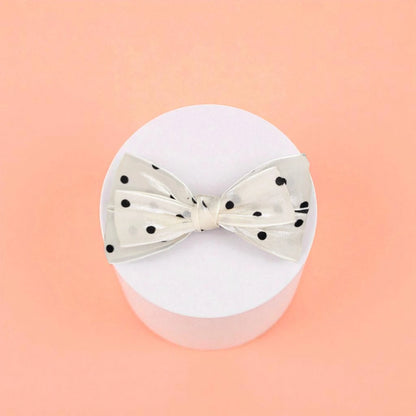 Bow with black polka dots on a white acrylic pedestal with a light background