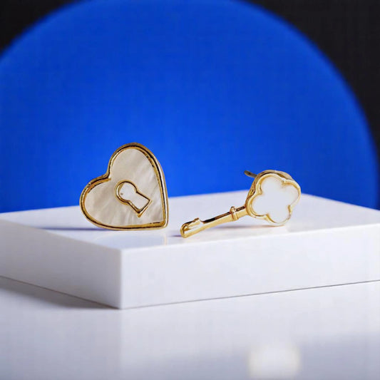 Gold heart and key-shaped earrings on a white display, set against a blue background. Stylish and playful jewelry design.