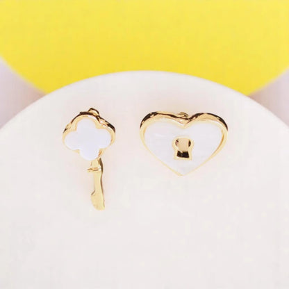 Gold and white stud earrings featuring a key and heart design, set against a yellow background.